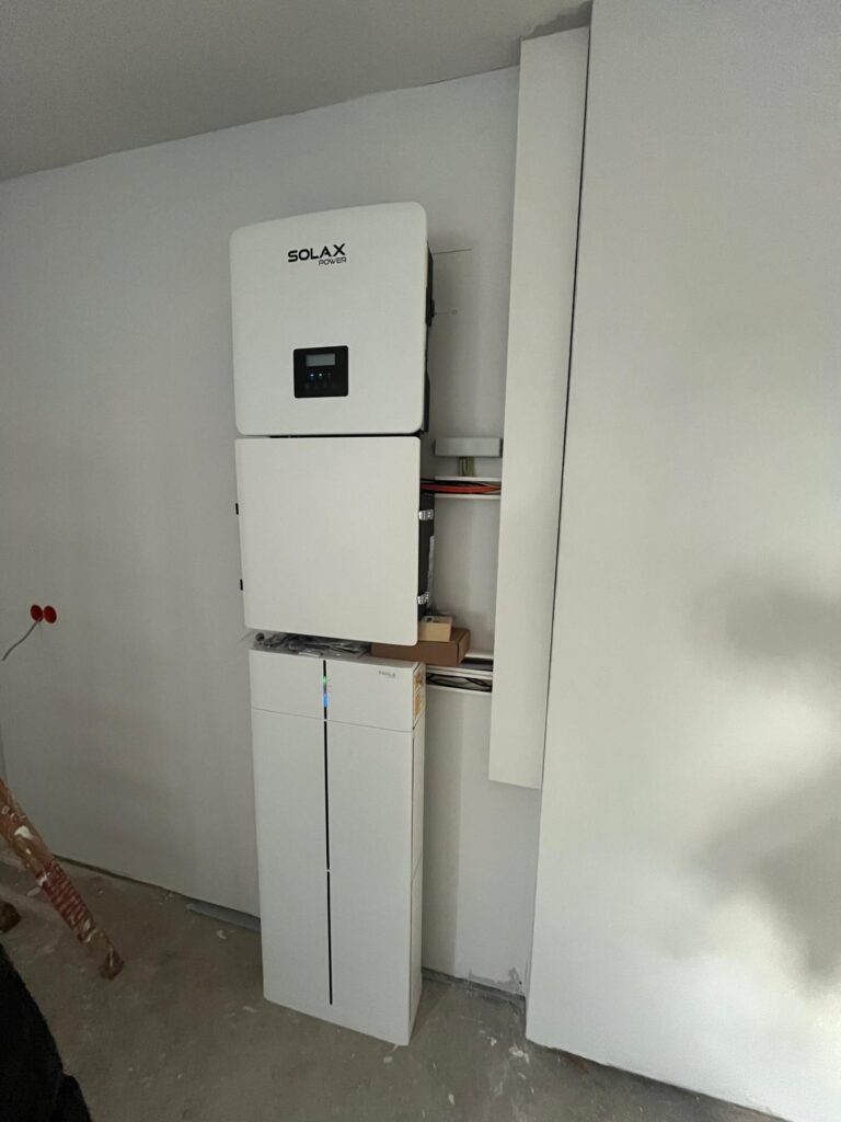 Weiße Solax-Power-Einheit an einer weißen Wand montiert, darunter ein weiteres weißes Gerät.