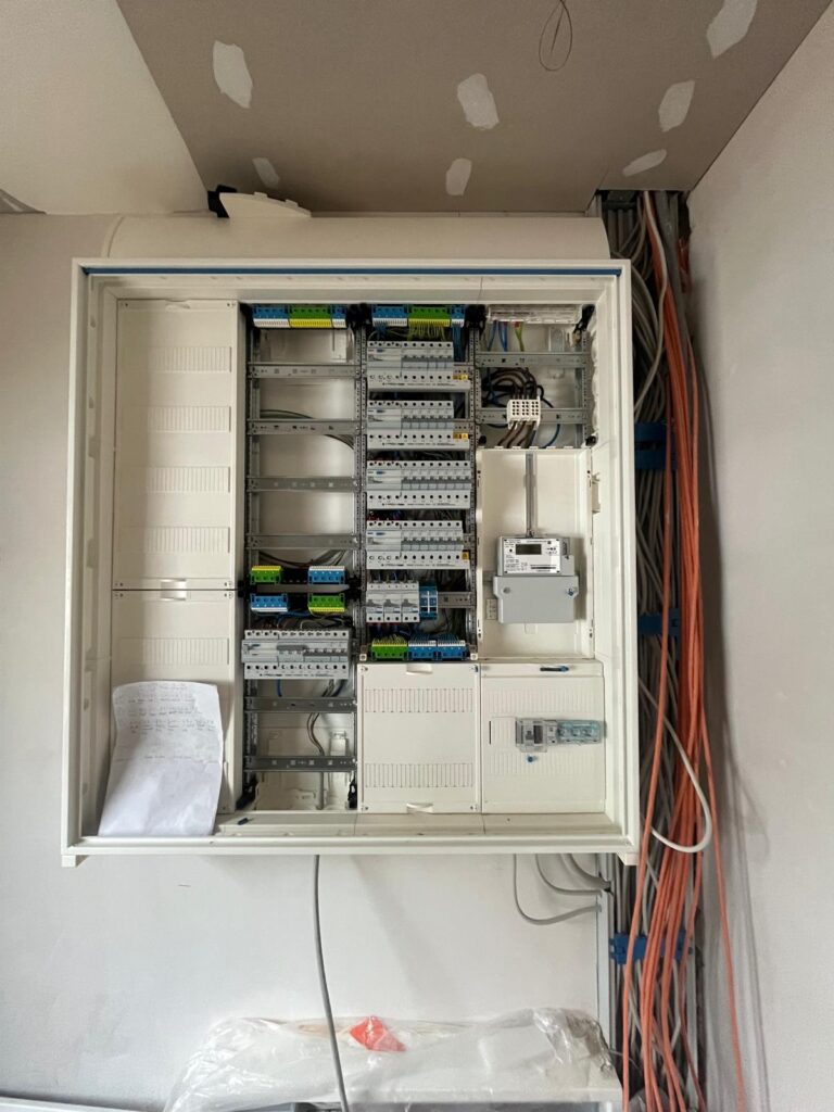 Offener Schaltschrank mit Kabeln, Sicherungen und Montageschienen, daneben hängende Kabelstränge.