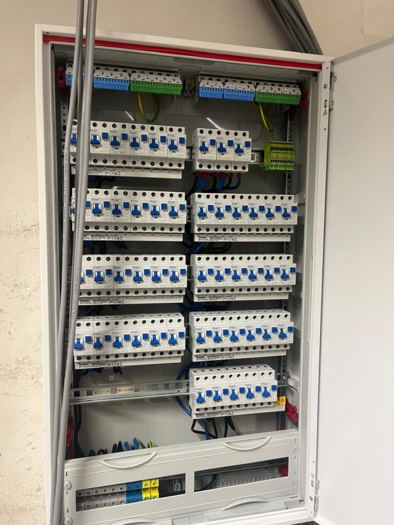 Offener Sicherungskasten mit mehreren Reihen von Schaltern und Kabeln im Inneren.
