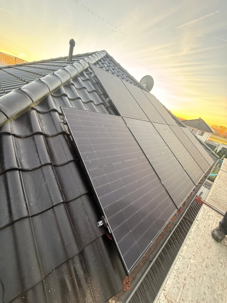 Dach mit Solarpaneelen bei Sonnenuntergang, schwarze Schindeln, daneben ein Baugerüst.