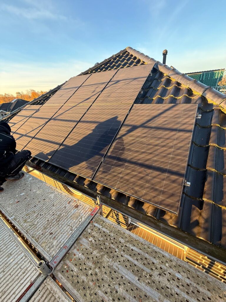 Solarmodule auf einem Ziegeldach, Gerüst im Vordergrund und blauer Himmel im Hintergrund.