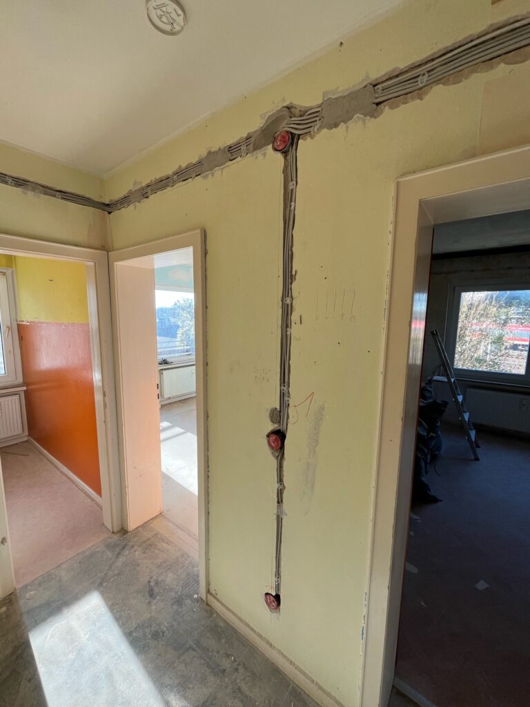 Gelber Raum mit offenen Wänden, sichtbaren Kabeln und runden Elektroinstallationsdosen.