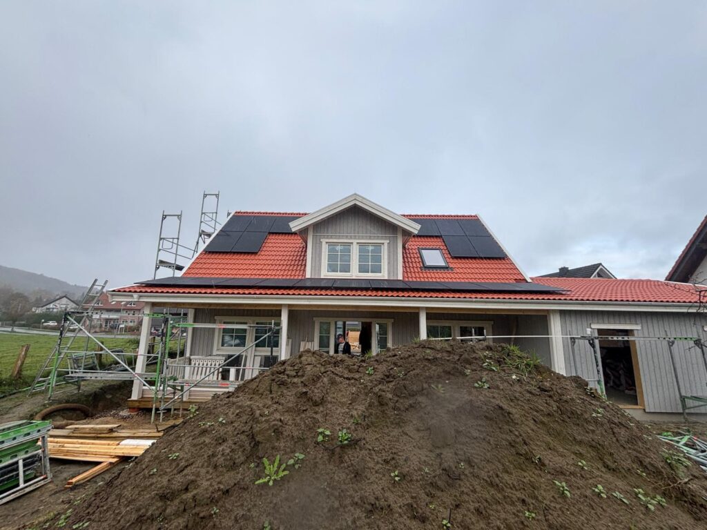 Haus mit roten Ziegeldach, Solarpanels, Baugerüst und Erdhügel im Vordergrund.